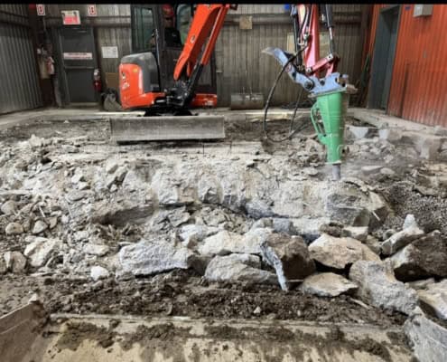 Concrete demolition with a mini-excavator breaker removing an industrial slab in Montreal
